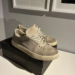 Sneaky Steve – Lescape Suede Shoe (stl 44) - Säljer ett par grå mockaskor från Sneaky Steve i storlek 44. Skorna är i bra skick och har varit väl omhändertagna. De är inte speciellt slitna utvändigt, men innersulan är något sliten. Modellen är stilren, bekväm och passar både till vardags och mer uppklädda outfits.  Skorna kommer med originalkartong, men kartongen är från en likadan modell i annan färg (den rätta kartongen finns inte kvar).  Nypris brukar ligga runt 1 199–1 399 kr.
