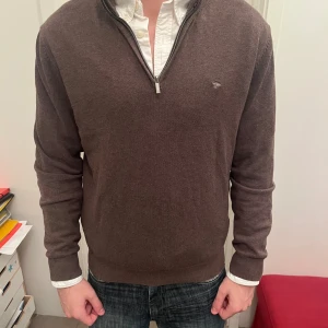 Brun half zip-tröja från Fynch-Hatton - Säljer en brun långärmad tröja från Fynch-Hatton med half zip och liten broderad logga på bröstet. Tröjan är i mjuk bomull och har ribbade muddar vid ärmslut och nederkant. Perfekt för lager-på-lager och chill stil.
