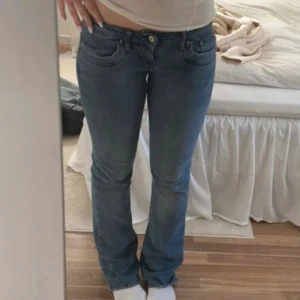 Blå bootcut jeans med låg midja - Säljer ett par klassiska blå jeans med låg midja och bootcut passform. Jeansen har fem fickor, dragkedja och knapp framtill. Perfekta för dig som gillar en tidlös look med lite utsvängda ben. Materialet är jeans i bomull. Strl 26/32