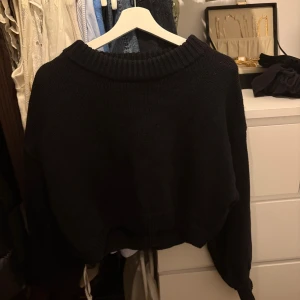 Svart stickad croppad tröja - Svart stickad tröja med croppad passform och bred ribbad krage. Tröjan har långärmade ärmar, från NAKD