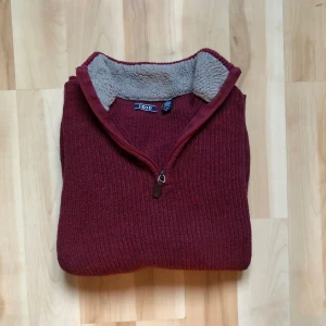 Vinröd stickad tröja från IZOD XL - Mysig vinröd stickad tröja från IZOD i storlek XL. Tröjan har en half zip-dragkedja och en krage fodrad med grå fleece för extra värme. Ribbstickade muddar och långärmad modell gör den perfekt för kyliga dagar.