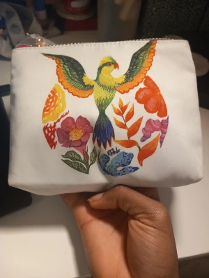 Vit necessär med färgglad fågel med hudvård - Snygg vit necessär från Estée Lauder i syntetmaterial med dragkedja och ett färgglatt tryck av en fågel och blommor på framsidan. Perfekt storlek för smink eller småprylar. Färgerna på trycket är bland annat gul, grön, orange, lila och blå. Innehåller en 30ml Perfectly Clean Multi-Action Foam Cleanser/Purifying Mask, två 7ml askar av Revitalizing Supreme+ Youth Power Creme och Revitalizing Supreme+ Night Intensive Restorative Creme (en av varje), och en 7ml Advanced Night Repair.