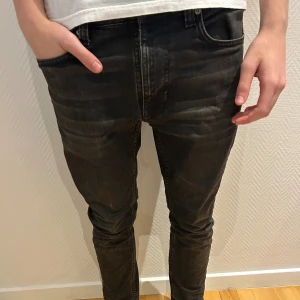 Svarta skinny jeans från Nudie Jeans - Hej 👋 Säljer ett par svarta jeans från Nudie Jeans med klassiska bakfickor och diskret logga. Jeansen har slim fit passform, normal midja och är tillverkade i mjukt denimtyg. Perfekta för dig som gillar en stilren och enkel look. Är ett litet hål längst ner vid kanten på byxorna som du ser på sista bilden men syns knappt. Hör av dig vi frågor och funderingar✅💬