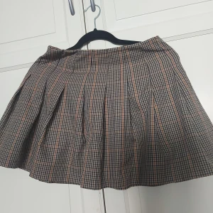 Rutig kortkjol från H&M Divided - ⚠️ Skriv till mig innan köp!⚠️Superfin rutig kortkjol från H&M Divided i beige, svart och brunt. Kjolen har klassiska veck och dragkedja i sidan för enkel påklädning. Perfekt för en trendig och preppy look.