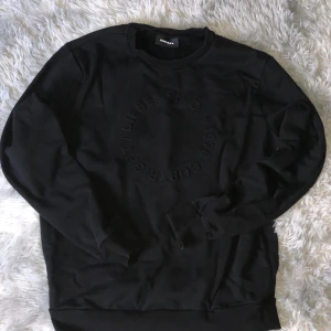 Svart sweatshirt från Diesel - Svart sweatshirt från Diesel med rund hals och diskret präglad logga i cirkel på bröstet. Tröjan är långärmad och har ribbade muddar vid ärmslut och nederkant. Tillverkad i mjuk bomullsblandning med polyester för extra komfort.