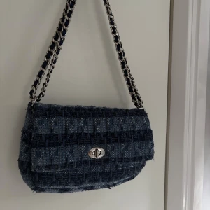 Väska från Becksöndergaard - Snygg axelväska från Becksöndergaard i mörkblått och ljusblått rutigt tyg. Väskan har en kedjerem med inslag av tyg och ett klassiskt vridlås i silver. Perfekt storlek för det viktigaste och ger en cool, trendig vibe till din outfit.