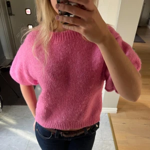 Rosa stickad kortärmad tröja - Superfin rosa stickad tröja med korta puffärmar och ribbad kant vid hals, ärmslut och nederkant. Modellen är lite croppad och har en loose fit som ger en avslappnad vibe