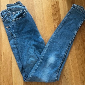 Blå slim Nudie Jeans - Säljer ett par blå slim jeans från Nudie Jeans i klassisk tvätt. Jeansen har fem fickor, orangea sömmar och snygga detaljer på bakfickorna. Modellen är slim och har normal midja. Perfekta för dig som gillar en slimmad look.