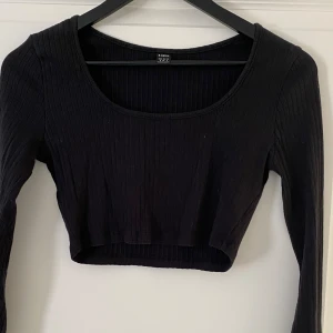 Svart ribbad croppad topp från SHEIN - Svart långärmad croppad topp från SHEIN i storlek S. Toppen är ribbad med rund halsringning och har en tight passform. Perfekt att matcha med höga jeans eller kjol för en trendig look.