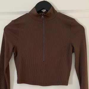 Brun ribbad croppad polotopp från SHEIN - Snygg brun croppad polotopp från SHEIN i storlek S. Toppen har ribbad struktur, lång ärm och en half zip-dragkedja framtill. Perfekt för dig som gillar stilrena och trendiga plagg med lite edge.
