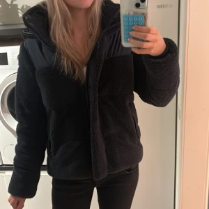 Svart teddyjacka med huva - Mysig svart teddyjacka med huva och quiltade detaljer upptill. Jackan är fluffig och har dragkedja framtill. Perfekt för kyliga dagar. Den är köpt från Zalando men är ifrån marikoo🩷