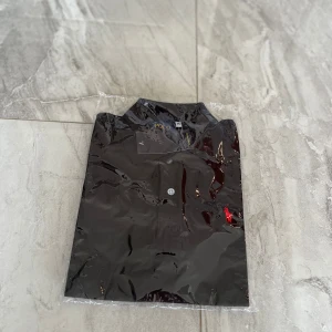 Svart Polo Ralph Lauren skjorta M - Svart skjorta från Polo Ralph Lauren i klassisk modell med krage och knappslå. Ikoniska röda loggan broderad på bröstet. Skjortan är tillverkad i bomull och har en stilren look som passar perfekt till jeans eller chinos.