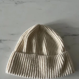 Ribbstickad beige mössa från H&M - Ribbstickad beige mössa från H&M i klassisk modell med uppvikt kant. Tillverkad i mjukt material som passar perfekt för kyliga dagar. Enkel och stilren design som funkar till de flesta outfits.