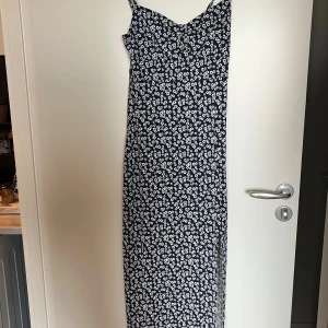 Blommig långklänning från Gina Tricot - Långklänning från Gina Tricot i marinblått med vita blommor. Klänningen har smala axelband, figurnära passform upptill. Använd en gång.