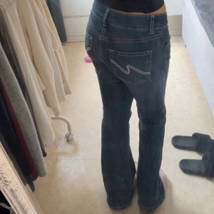 Mörkblå bootcut jeans med glitter - Snygga mörkblå jeans med bootcut passform och glittriga detaljer längs benen. Jeansen har låg midja och klassiska fickor med kontrastsömmar bak. Perfekta för dig som vill ha en cool och trendig look.