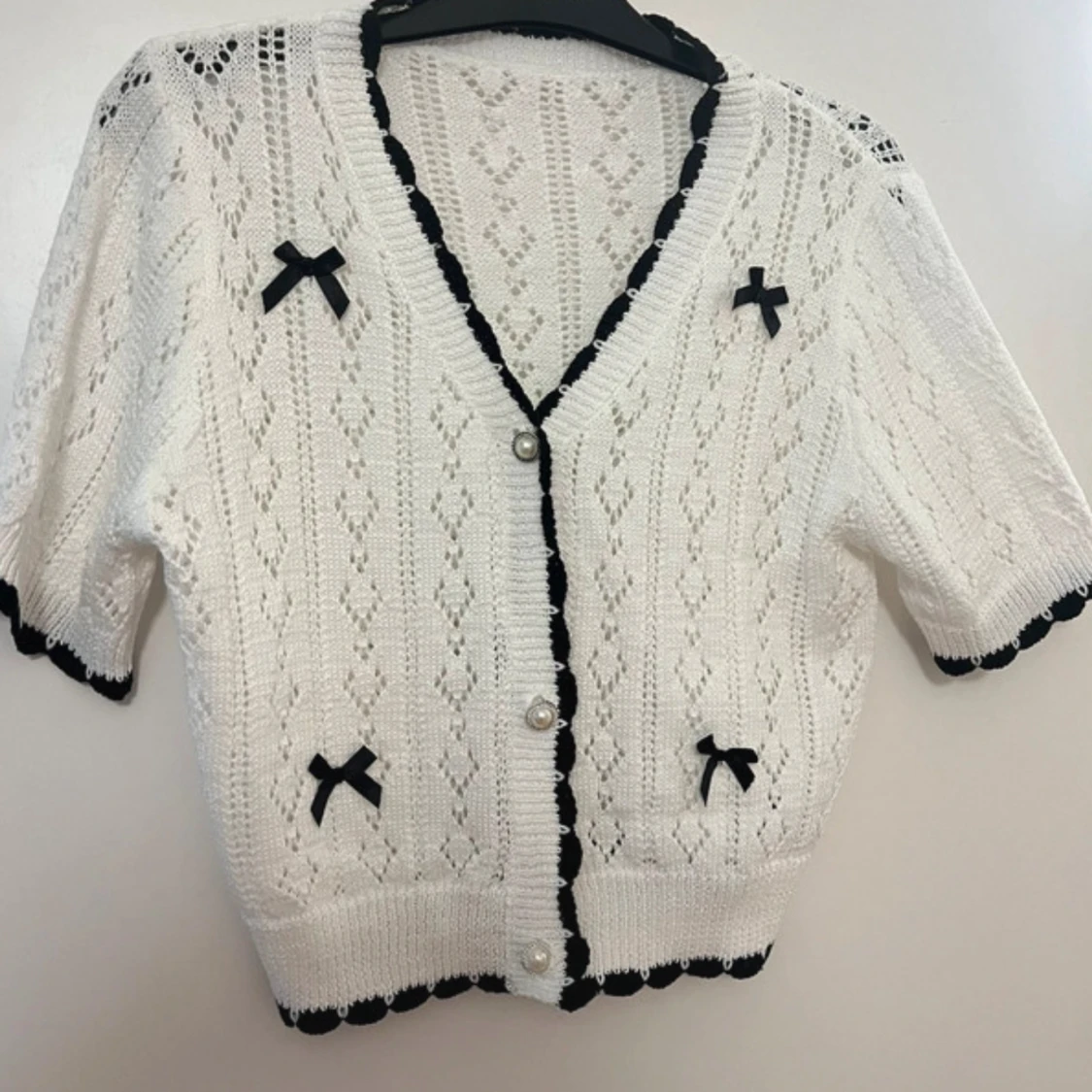 Vit stickad kofta med svarta rosetter