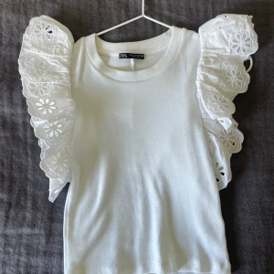 Vit fest topp med broderade volanger - Sjukt snygg vit fest topp från Zara med broderade volanger. Använd endast 1-2 gånger då den inte riktigt passar och sitter som jag vill att den ska sitta. Passar till allt och går inte att köpa längre. Priset kan diskuteras!