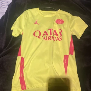 PSG Messi 30 gul matchtröja Nike - Gul PSG fotbollströja med Messi 30 på ryggen, tillverkad i lätt Dri-Fit material från Nike. Tröjan har korta ärmar, rosa tryck med Qatar Airways och Paris-detaljer samt Jordan-logga på bröstet. Perfekt för dig som vill sticka ut på planen eller supporta PSG.