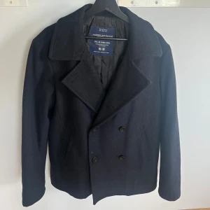 Svart skepparkavaj från American Eagle - Klassisk svart skepparkavaj från American Eagle med bred krage och dubbelknäppning. Jackan har två snedställda fickor framtill och är fodrad med quiltat innerfoder. Perfekt för kyliga dagar och ger en stilren look. Vid frågor och funderingar är det bara att skicka ett meddelande! Pris går att diskuteras!!