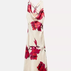 Vit långklänning med röda blommor - Säljer en elegant långklänning i vit ton med stora röda blommor. Klänningen har en snygg omlott-detalj vid halsen och är ärmlös med öppen rygg. Materialet känns lätt och flowy, perfekt för varma dagar. Passformen är normal och klänningen har en feminin siluett.