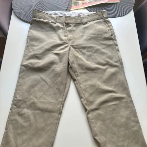 Beiga Dickies Slim Straight chinos - Säljer ett par beiga Dickies Slim Straight chinos med klassisk rak passform. Byxorna har hällor för bälte, två bakfickor och är tillverkade i slitstarkt bomullsmaterial. Perfekta för en clean och stilren look.