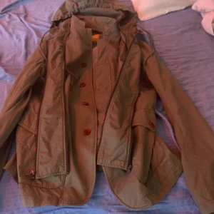 Grön parkajacka från Hugo Boss - Snygg grön parkajacka från Hugo Boss med huva och både dragkedja och knappar framtill. Jackan har praktiska fickor med lock och en clean design som funkar till många stilar. Materialet är slitstark bomull och jackan har långärmade ärmar.