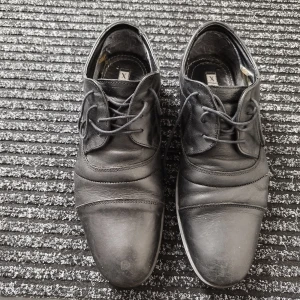 Svarta skinnskor från XIT, storlek 43 - Säljer ett par klassiska svarta skinnskor från XIT i storlek 43. Skorna har snörning, rund tå och låg klack. Perfekta för dig som vill ha en stilren och tidlös look. Tillverkade i skinn med diskreta sömdetaljer för extra stilpoäng.