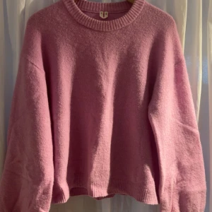 Rosa stickad tröja med loose fit - Mysig rosa stickad tröja med rund halsringning och ribbade muddar. Tröjan har en loose passform och långa ärmar, perfekt för lager på lager under kyliga dagar. Enkel och stilren design som är lätt att matcha.