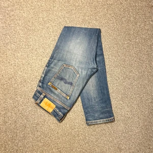 Nudie Lean Dean jeans i storlek W29/L30 - Nudie Lean Dean jeans i storlek W29/L30. Mörkblå denim med slim fit-passform och stretch som gör dem bekväma. Bra skick utan hål eller fläckar, bara lite slitningar. Nypris runt 1500–2000 kr.  Mått: A (midja): 40 cm B (lårvidd): 26 cm C (fotvidd): 16 cm D (innerbenslängd): 76 cm  Säljes för 399 kr.   