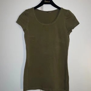 Olivgrön kortärmad topp - En enkel och stilren olivgrön topp med rund halsringning och korta ärmar. Modellen är figurnära och passar perfekt till jeans eller kjol. Tillverkad i mjuk bomull som känns skön mot huden.