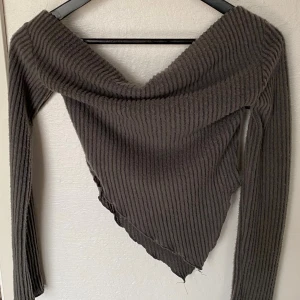 Mörkgrå ribbad topp från SHEIN - Säljer en mörkgrå ribbad topp från SHEIN med lång ärm och snygg omlott-vibb framtill. Toppen har en bred v-ringning och asymmetrisk nederkant som ger en cool look. Materialet är mjukt och stretchigt, perfekt för att sticka ut lite extra.