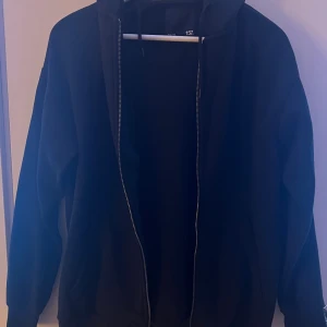 Svart hoodie med dragkedja från 157 - Svart hoodie från 157 i storlek M. Tröjan har huva, långa ärmar och dragkedja framtill. Perfekt för chill dagar eller när du vill ha något bekvämt. Klassisk och enkel design utan mönster.