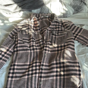 Rutig overshirt från H&M i rosa och svart - Overshirt från H&M i rosa och svart rutigt mönster. Skjortan har klassisk krage, knäppning framtill med silvriga knappar och två bröstfickor.