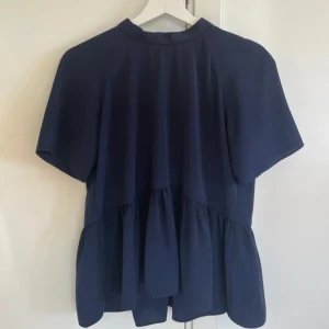 Marinblå blus med öppen rygg - En marinblå blus med öppen rygg och knytning. Blusen är i strl M, använd en gång och kommer från märket ”envii”.