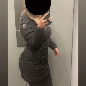 Parajumper irene jacket - Säljer en svart, lång och lätt dunjacka från Parajumpers i storlek S. Jackan har huva, dragkedja framtill och klassisk Parajumpers-logga på ärmen. Perfekt för kalla dagar och riktigt snygg passform. Ena dragkedjan på fickan högre upp är sönder (se sista bild) , men inget som förstör hur jackan ser ut på och går säkert att fixa för en billigare peng!