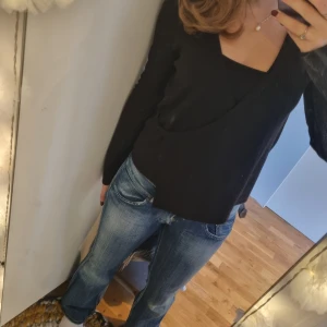 Svart omlottkofta med knyt i sidan - Svart omlottkofta med knyt i sidan och v-ringad hals. Koftan är ribbad och har långa ärmar. Perfekt att slänga över ett linne eller t-shirt för en chill look. Materialet känns mjukt och stretchigt.