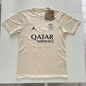 PSG x Jordan beige fotbollströja S Dembele #10 - Säljer en beige PSG fotbollströja i samarbete med Jordan, storlek S. Tröjan har korta ärmar, svart tryck med Qatar Airways och klubbmärke fram, samt O. Dembélé och nummer 10 bak. Tillverkad i Dri-Fit material för bästa komfort.