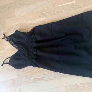 Svart spetsklänning med smala axelband - Supersöt svart klänning med smala axelband och v-ringning. Klänningen har fina spetsdetaljer både vid urringningen och i midjan, samt en lätt rynkad kjol. Perfekt för dig som gillar en feminin och stilren look.