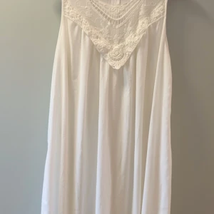 Vit ärmlös gravidklänning från Mamalicious - Superfin vit gravidklänning från Mamalicious i storlek L. Klänningen är ärmlös med vackra spetsdetaljer upptill och har en lös, rak passform som ger plats åt en växande mage.. Går enkelt att piffa till med ett bälte. Perfekt för sommarens varma dagar och har en elegant, enkel look med broderad spets vid halsen.