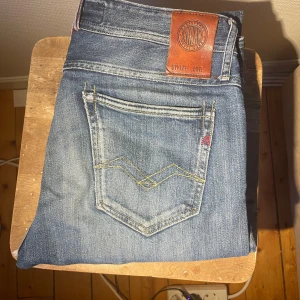 Replay  ljusblå jeans - Snygga ljusblå Replay Anbass jeans med klassisk femficksdesign och gul kontrastsöm på bakfickan. Jeansen har en läderpatch med Replay-logga i midjan och är tillverkade i mjukt jeansmaterial. Perfekt för dig som gillar stilrena och bekväma jeans. Hål på knät