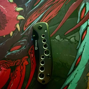 FAKE kn!v - Fällkn!v med svart blad och greppvänligt handtag med dekorativa hål. Mycket gott skick utan synligt slitage. Perfekt för friluftsliv eller vardagsbruk. Kompakt och lätt att bära med sig.