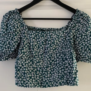 Grön blommig blus från H&M Divided - Supersöt grön blus med vita små blommor från H&M Divided. Modellen är croppad med puffiga korta ärmar och resår vid hals och ärmslut. Perfekt för vår och sommar när du vill ha en chill och trendig look.