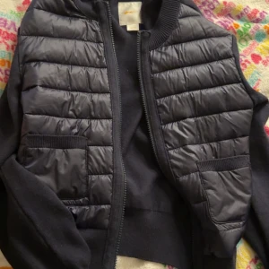 Svart quiltad dunväst från Gina Tricot - Svart dunväst från Gina Tricot i storlek 158/164. Västen har quiltade paneler, två fickor framtill och dragkedja. Snygg och enkel design som funkar till många olika outfits. Liknar monclears jacka 