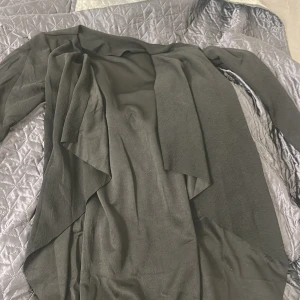 Svart omlott kappa med knytband - Säljer en svart lång kappa i omlottmodell med knytband i midjan och stora fickor framtill. Jackan har långa ärmar och ett snyggt, draperat fall framtill. Perfekt för dig som gillar en stilren och enkel look.