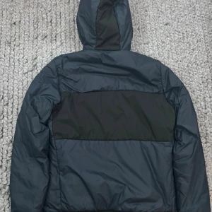 Mörkblå pufferjacka från Sail Racing - Säljer en mörkblå pufferjacka från Sail Racing med svarta detaljer och huva. Jackan har dragkedja framtill, en bröstficka med logga och två sidofickor. Perfekt för kyliga dagar och riktigt snygg streetstil. Felfri och varsamt använd