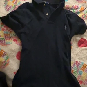Marinblå pikétröja från Polo Ralph Lauren - Snygg marinblå pikétröja från Polo Ralph Lauren i slim fit-modell. Tröjan har klassisk krage, två knappar framtill och den ikoniska broderade loggan på bröstet. 