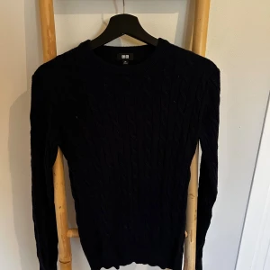 Mörkblå kabelstickad tröja Uniqlo XS - Säljer en mörkblå kabelstickad tröja från Uniqlo i storlek XS. Tröjan har rund halsringning och långa ärmar, perfekt för lager-på-lager under kyliga dagar. Klassisk och enkel design som funkar till det mesta.