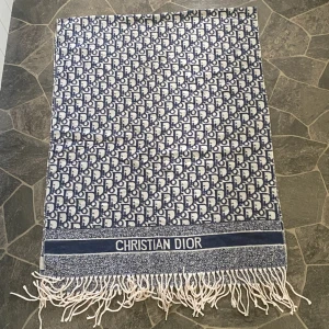 Blåvit halsduk från Christian Dior - Snygg halsduk från Christian Dior i blått och vitt med klassiskt logomönster över hela tyget. Halsduken har fransar i ändarna och en bred kant med Christian Dior-tryck. Perfekt accessoar för att lyfta din outfit.