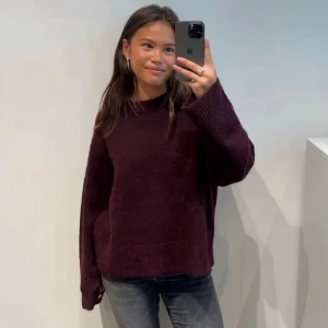 Vinröd stickad oversized tröja - Säljer en stickad tröja i vinröt. Tröjan har långa ärmar och en avslappnad passform med breda muddar vid ärmsluten. Perfekt för lager-på-lager och chill dagar.