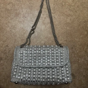 Glittrig silver axelväska med kedja - Supersnygg axelväska i silver med glittriga stenar och kedjerem. 